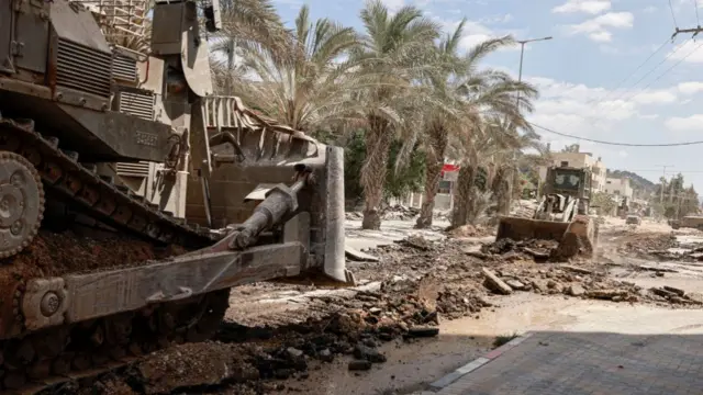 Two bulldozers are seen driving down a road as rubble from the road is pulled up