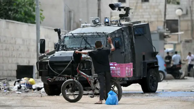 A Palestinian boy raises his arm into the air as Israeli soldiers inspect what he is carrying during a raid in Jenin in the occupied West Bank on August 28, 2024