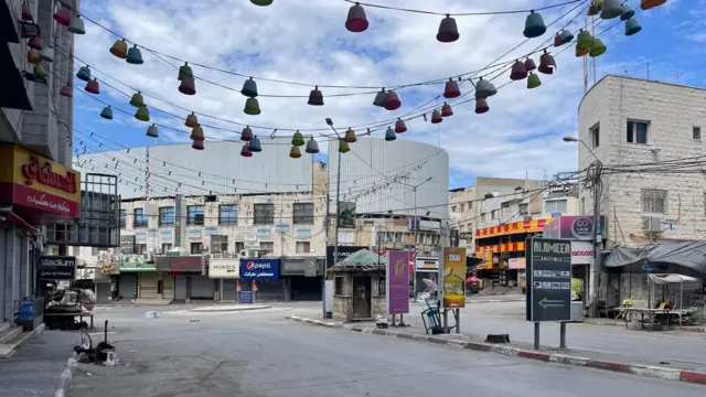 An empty street in Jenin, the shops are all closed with their shutters down and there are no cars or people on the road