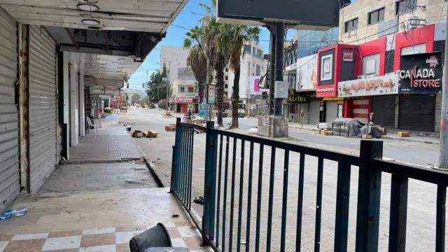 An empty street in Jenin, the shops are all closed with their shutters down and there are no cars or people on the road