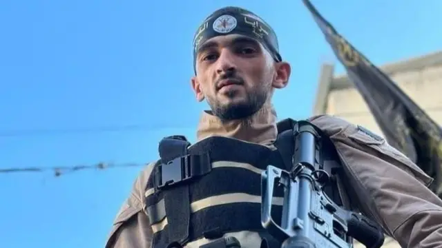 Abu Shujaa, wearing a PIJ headband, military clothes and carrying an M4-style assault rifle