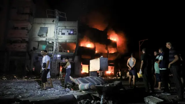 Palestinians gather at the site of an Israeli strike on a house, which is on fire