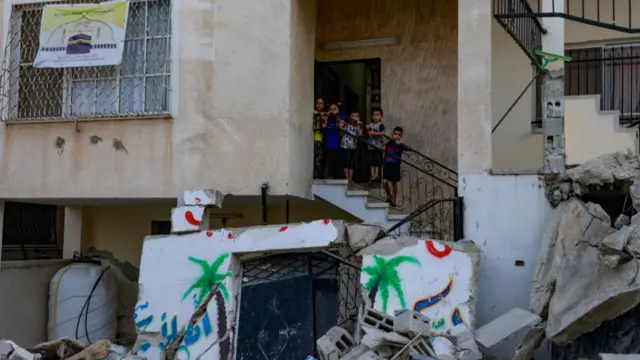 Palestinian children line up on the stairway of a house, surrounded by rubble