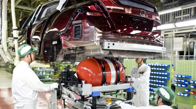 Three mechanics working on a car in a Honda factory