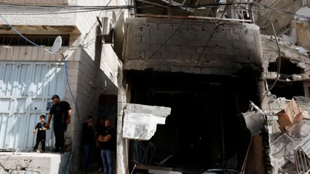 A group of people including a child stand next to a burn out building