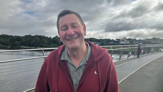 A man with brown hair wearing a green shirt and red jacket