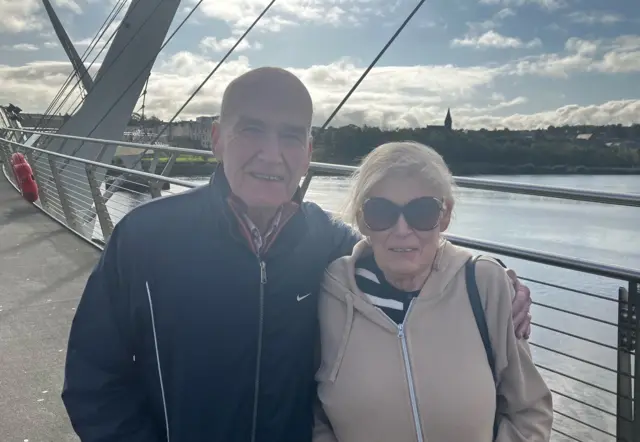 A man wearing a navy coat. A woman wearing a tan jacket with blonde hear and wearing sunglasses.