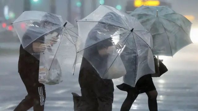 Three pedestrians holding umbrellas battling winds