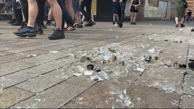 Smashed glass on the floor, with people walking by