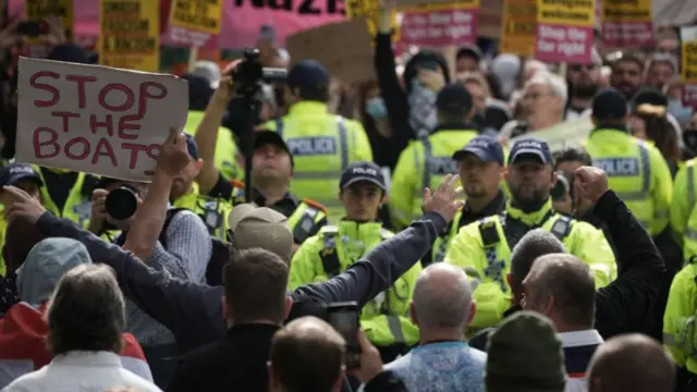 Protesters with placards "Stop the Boats" in front of a police line and an anti-racism protest