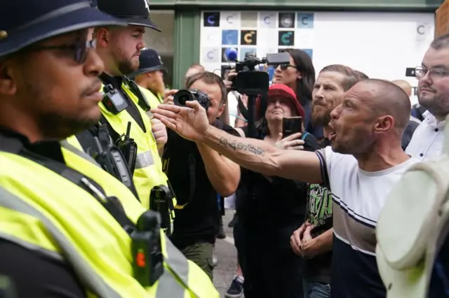 Protestor stretching out his arm to the chest of a police officer standing in a crowd of protestors