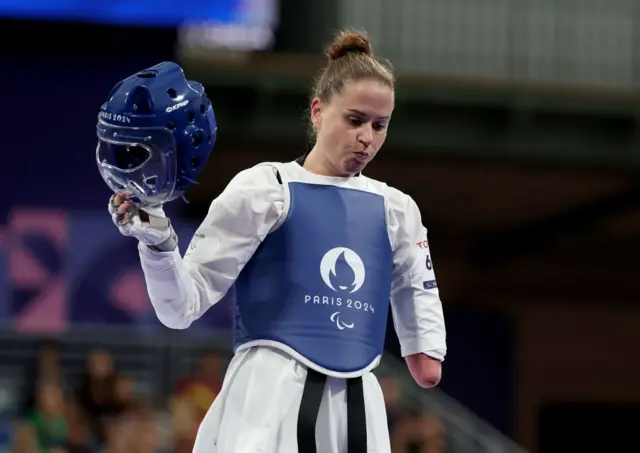 Beth Munro takes off her helmet and looks disappointed after losing her Para-taekwondo quarter-final