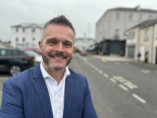 Robbie Butler on a street smiling in a navy suit jacket and white shirt