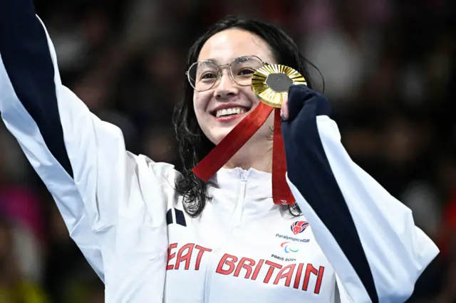 Alice Tai holds up her medal on the podium