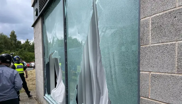 A smashed window at a hotel in Rotherham, a man and a police officer are stood nearby