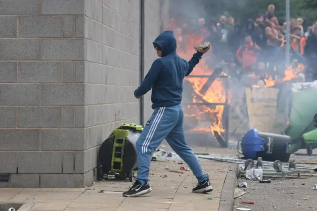 A man throwing a brick with a fire behind him