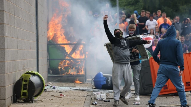 A man with arms raised in front of a fire at a demonstration