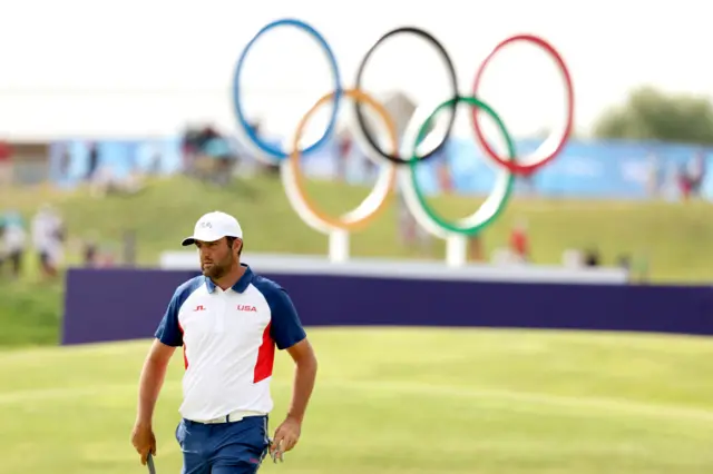 Scheffler prepares to take a putt in front of the Olympic rings