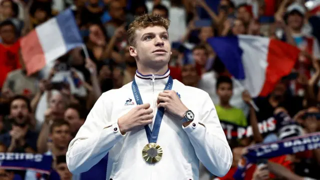 Léon Marchand holds a medal in front of a sea of French fans