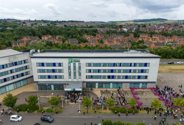 An areil view of the Holiday Inn Express in Rotherham. Pro and anti immigration demonstrators are outside, separated by a purple barrier.