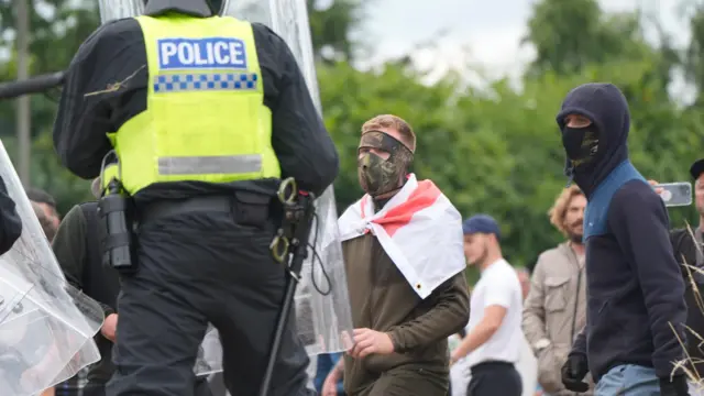 Two masked men - one draped in an England flag - challenge police during violence outside a hotel in Rotherham.