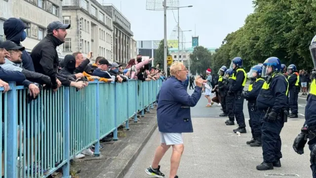 A man stands in between a group of protesters and riot police