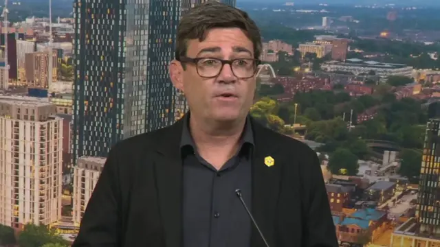 Ο Andy Burnham φορώντας ένα μαύρο σακάκι και μαύρο πουκάμισο