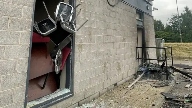 Chairs and tables pushed against a broken window