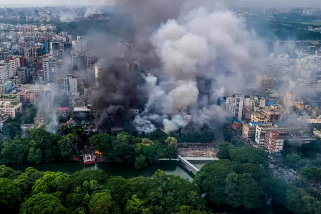 Huge plumes of smoke rising from builsings. The photo has been taken from a distance above.