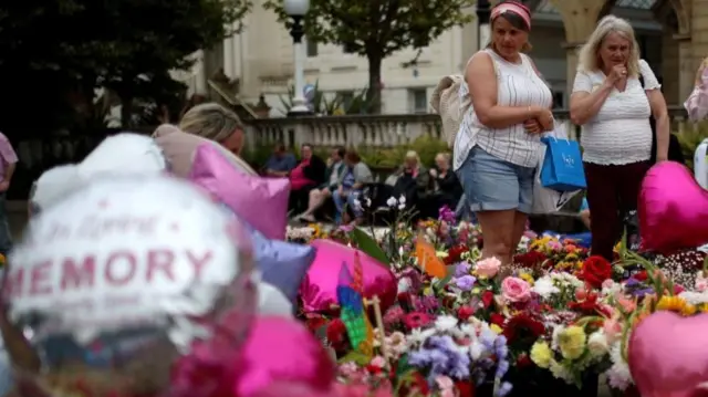 Two people look at a floral tribute and balloons at a vigil for the Southport stabbings