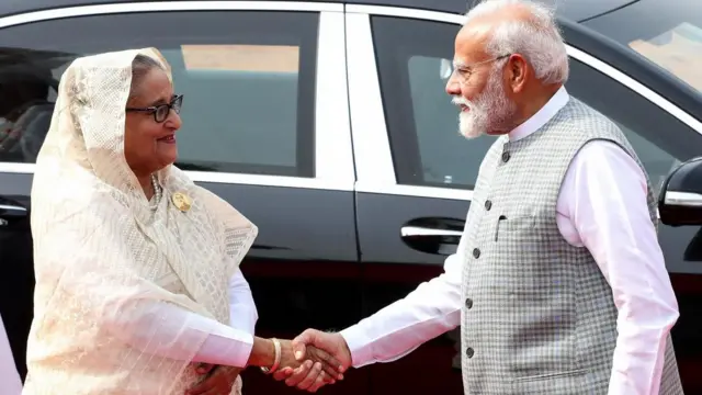 Bangladesh Prime Minister Sheikh Hasina  shaking hands with Indian PM Narendra Modi, there is a car in the background.