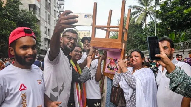 A group poses with a chair looted from Sheikh Hasina's residence.