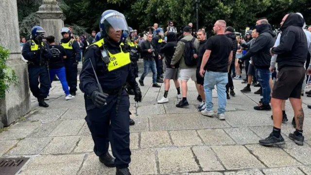 A number of officers and a police dog face protestors in Guildhall Square