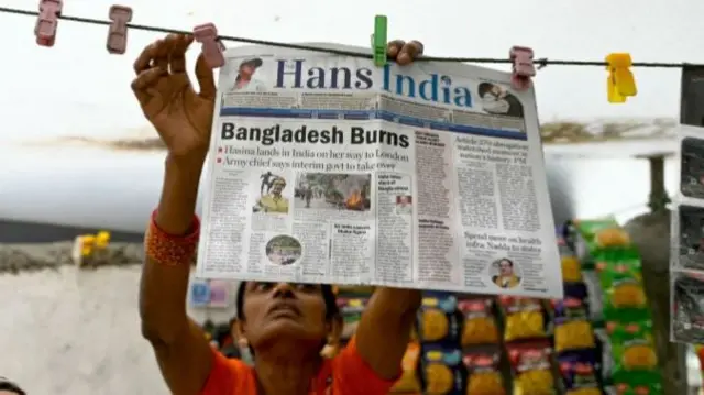 A vendor hangs a newspaper with the front page article reading 'Bangladesh Burns' along a roadside in Hyderabad.