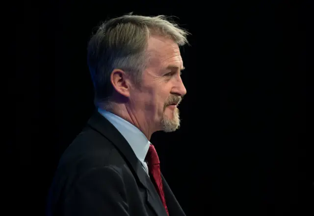 Huw Irranca-Davies in a suit and tile on a dark background