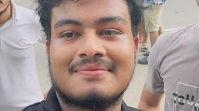 A bearded man with black hair in a black polo shirt smiles into the camera.