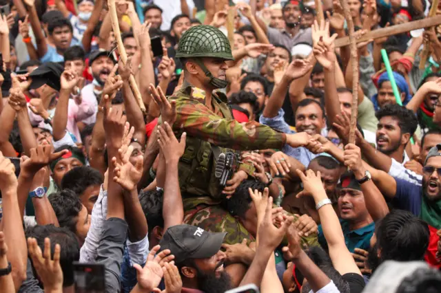 A soldier is carried through a crowd of cheering protesters on someone's shoulders.