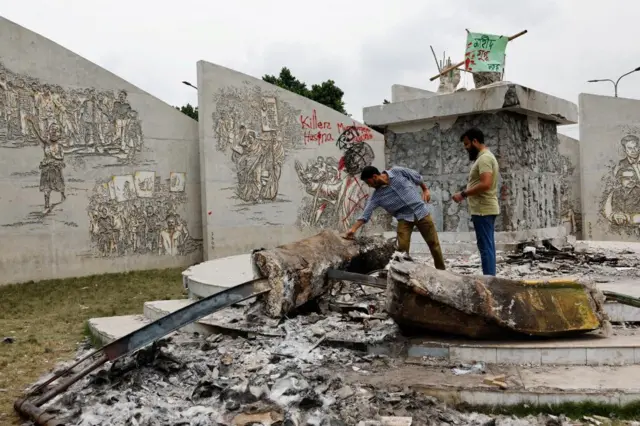 Two men look down at a fallen statue in front of walls of graffiti