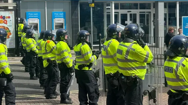 A line of riot police wearing shields and helmets