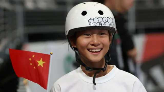 Zheng Haohao smiles while holding a China flag at the Olympic Qualifier Series event in Shanghai in 2024