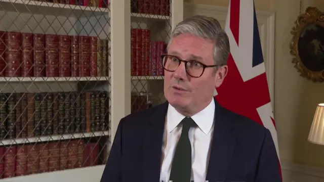 Keir Starmer giving an interview, he is in front on a book case and Union Jack