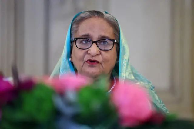 Head shot of Sheikh Hasina, slightly hidden behind some out-of-focus flowers