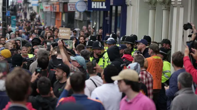 A crowd of protesters on a street. A line of police seperate them from others