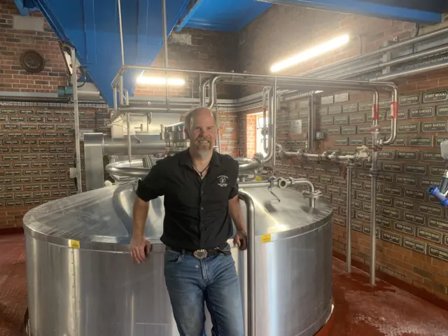 Head brewer Buster Grant standing in front of brewing equipment with pipes in the background