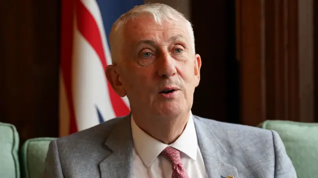 Lindsay Hoyle sits on a green sofa in front of a the UK's flag