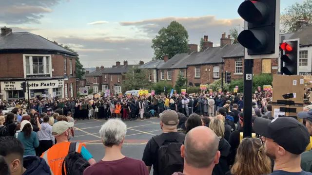 A crowd of around 1,500 people gather in Sheffield, standing at a street with a pantry in the background.