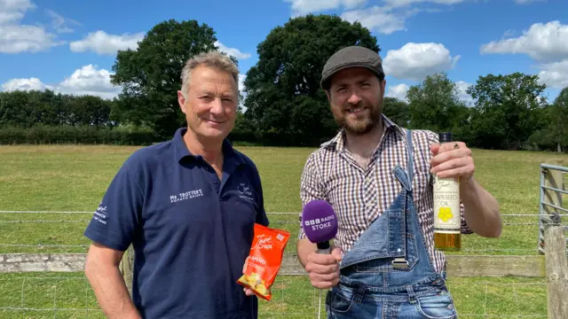 Anthony Froggart stands in a field holding a pack of his crisps, with BBC Radio Stoke’s Matt Weigold holding Just Oil's rapeseed oil.