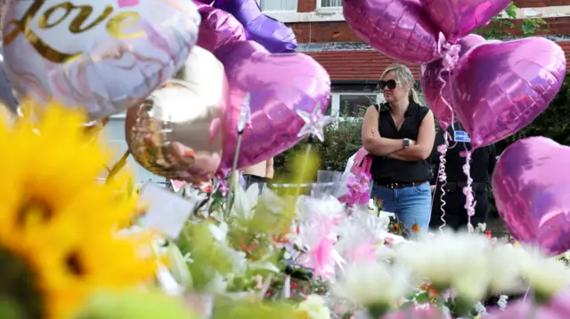 A woman looks at the floral tributes and stuffed toys laid out in memory of Elsie Dot Stancombe, Bebe King and Alice Dasilva Aguiar