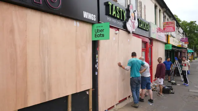 Men with a stepladder and tools board up shops along a street