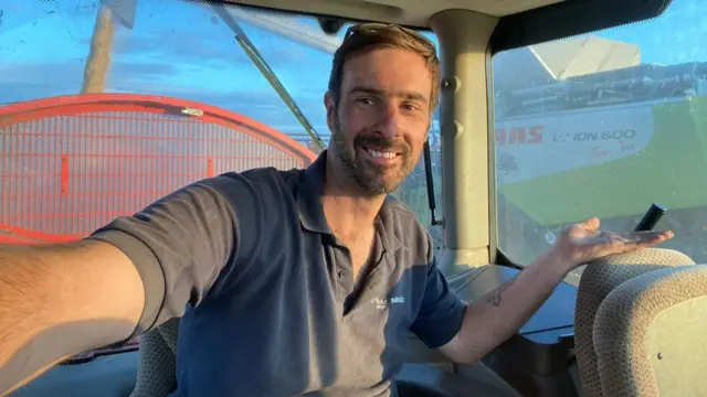 Luke sits in the cab of a harvesting machine